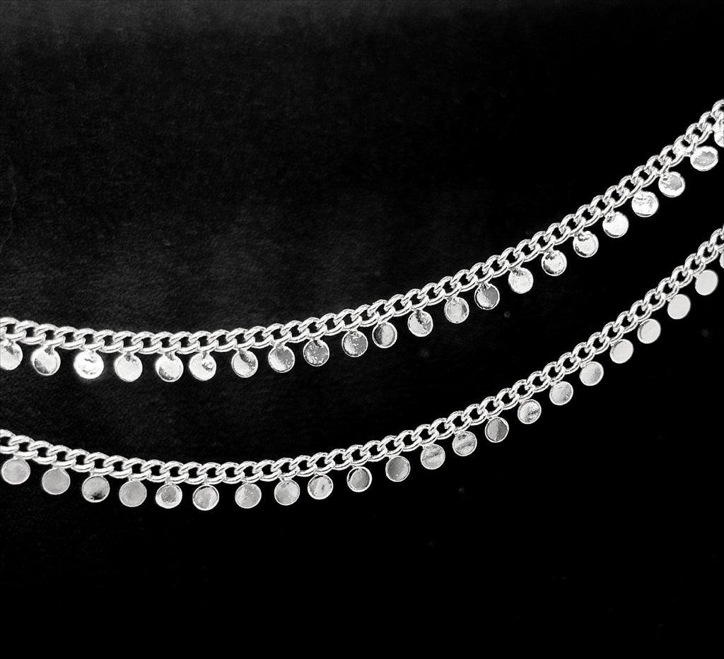 Silver disc chain with small flat circular disc charms on a black background.