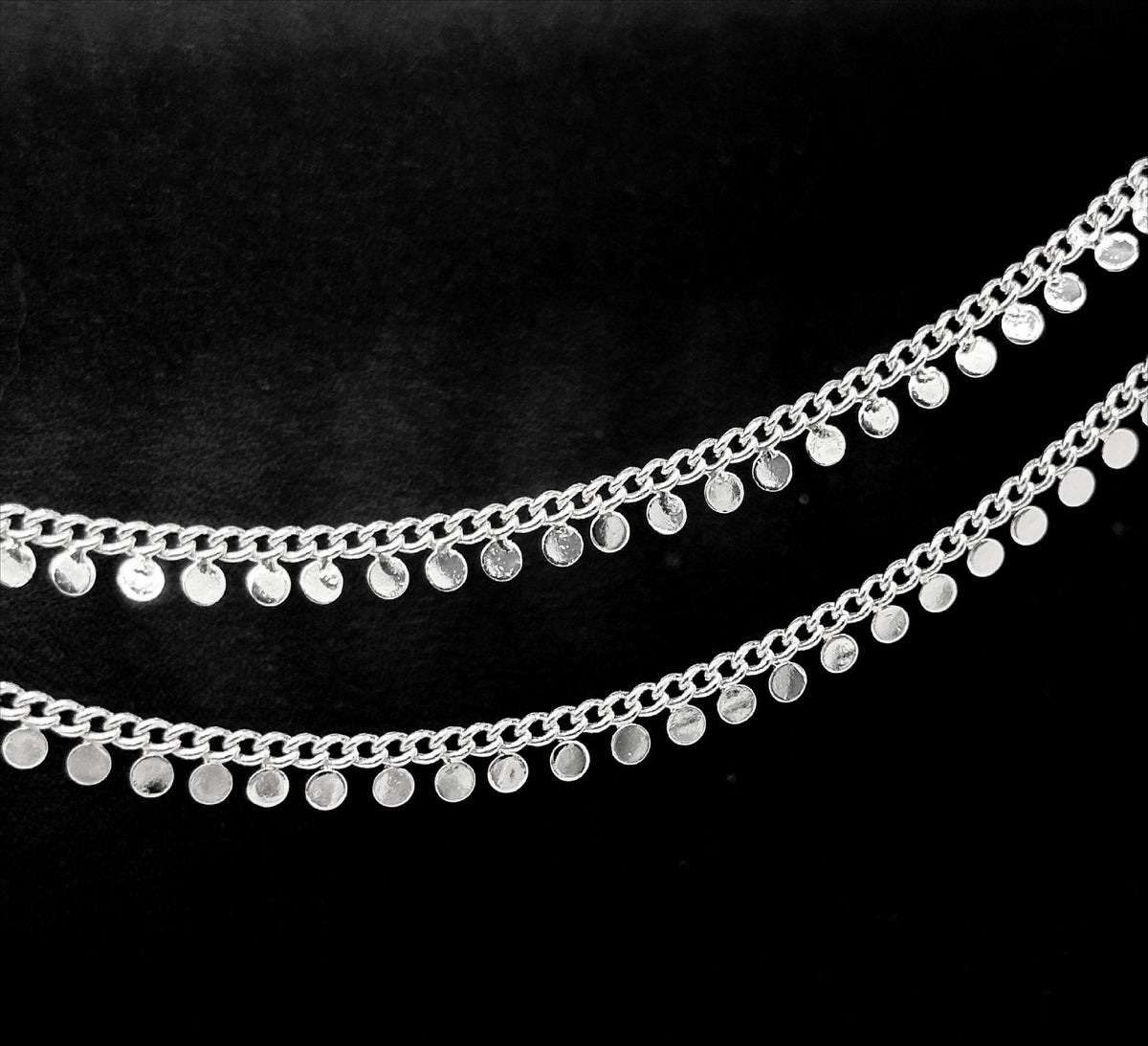 Silver disc chain with small flat circular disc charms on a black background.