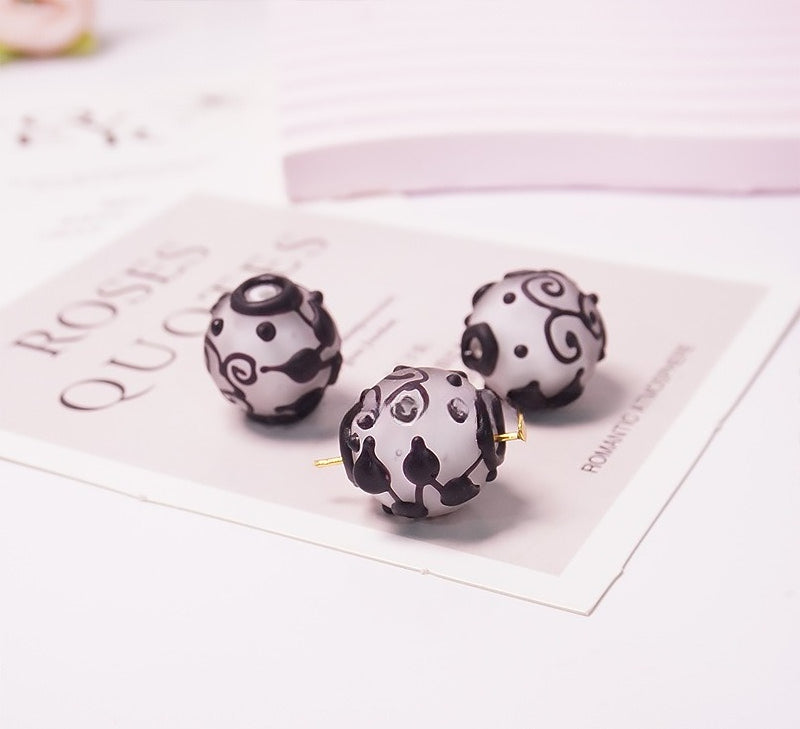 Three round black and white patterned bead earrings displayed on a decorative card on a white surface.
