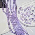 Purple faceted glass beads on cords arranged on white spiral tray