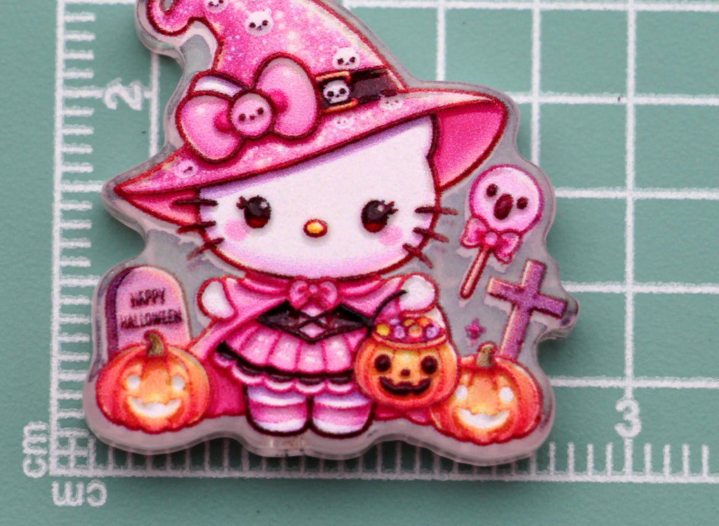 Hello Kitty pink wizard acrylic charm with witch hat, pumpkins, skull lollipop, and tombstone on green cutting mat