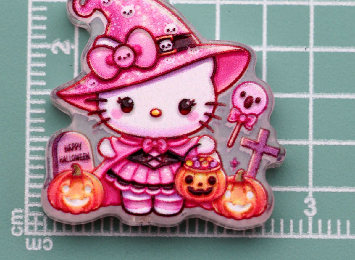 Hello Kitty pink wizard acrylic charm with witch hat, pumpkins, skull lollipop, and tombstone on green cutting mat