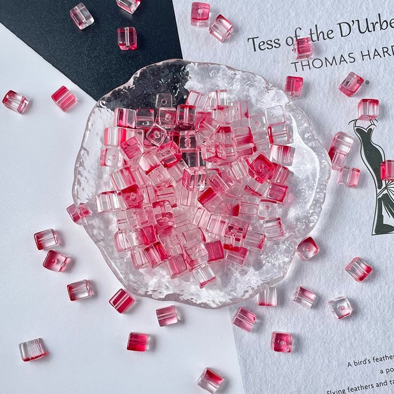 Clear cube glass beads with pink and red accents in glass dish on white