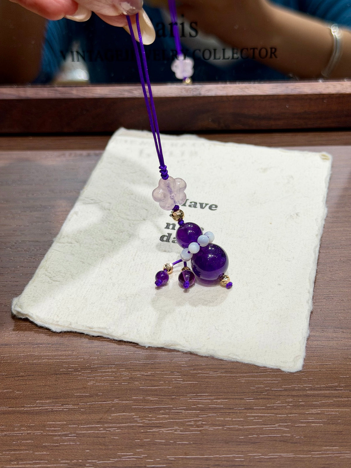 Hand holding amethyst fortune gourd charm with cat's eye shell beads