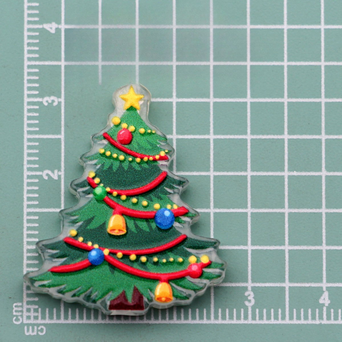 Christmas tree acrylic charm with red garland, star topper, and colorful ornaments on green cutting mat