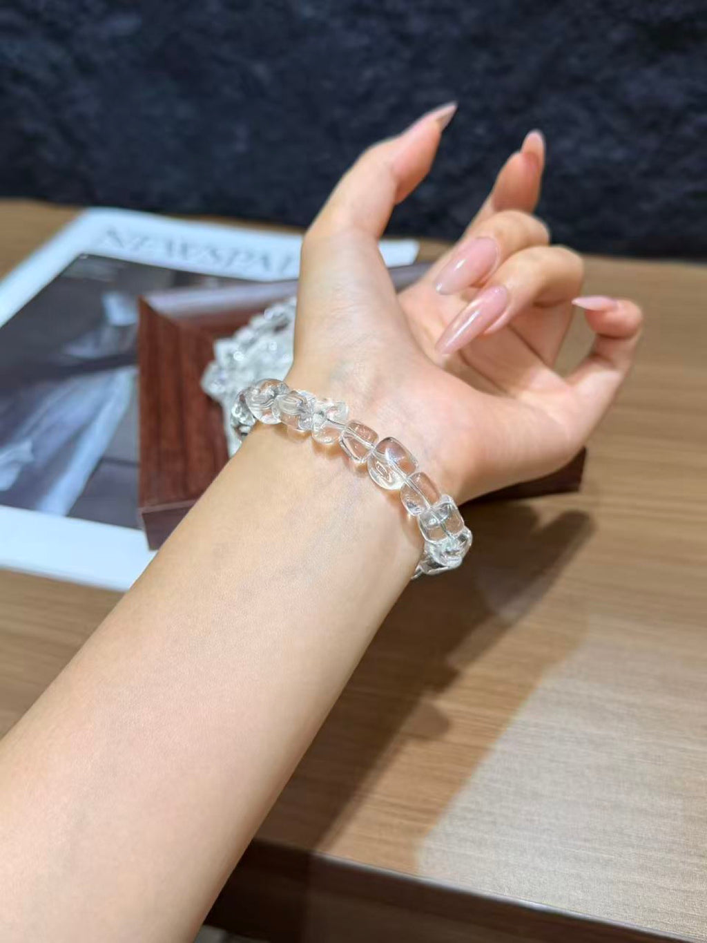 White quartz jelly-bean nugget bracelet worn on a wrist, with a wooden gift box and magazine in the background