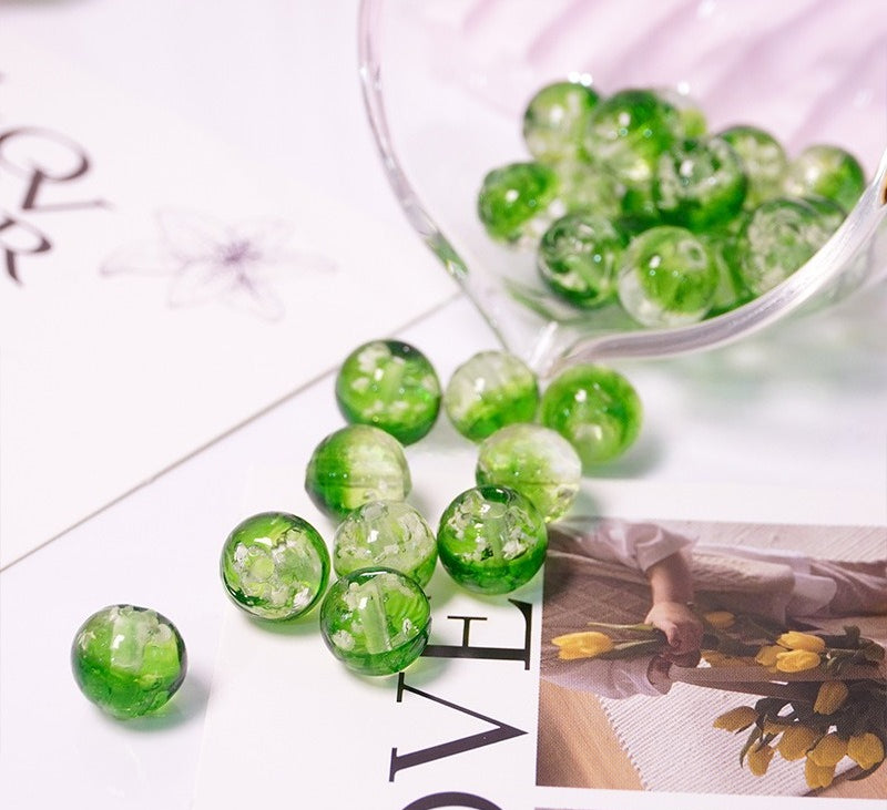 Green two-tone glow-in-the-dark glass beads spilling from a glass cup onto a printed card