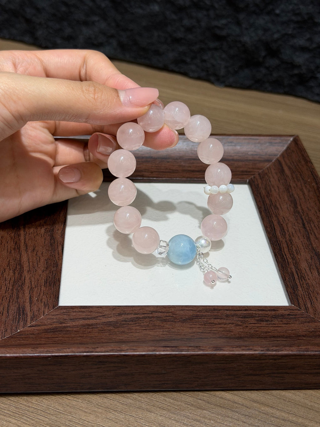 Hand holding peach mist bracelet with pink quartz over tray