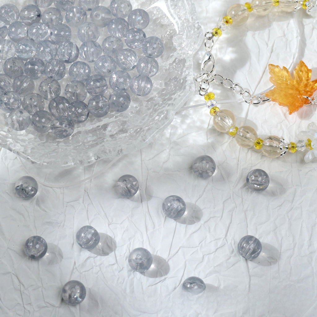 Clear glass bead bracelet with leaf charm beside a bowl of loose beads