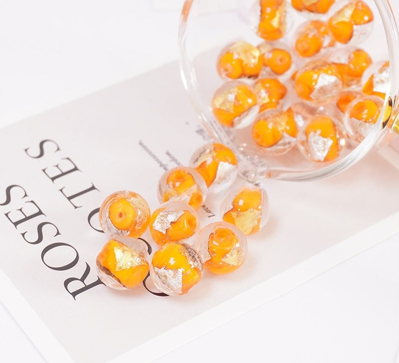 Orange and gold-flake glass beads spilling from a glass bowl onto a printed card