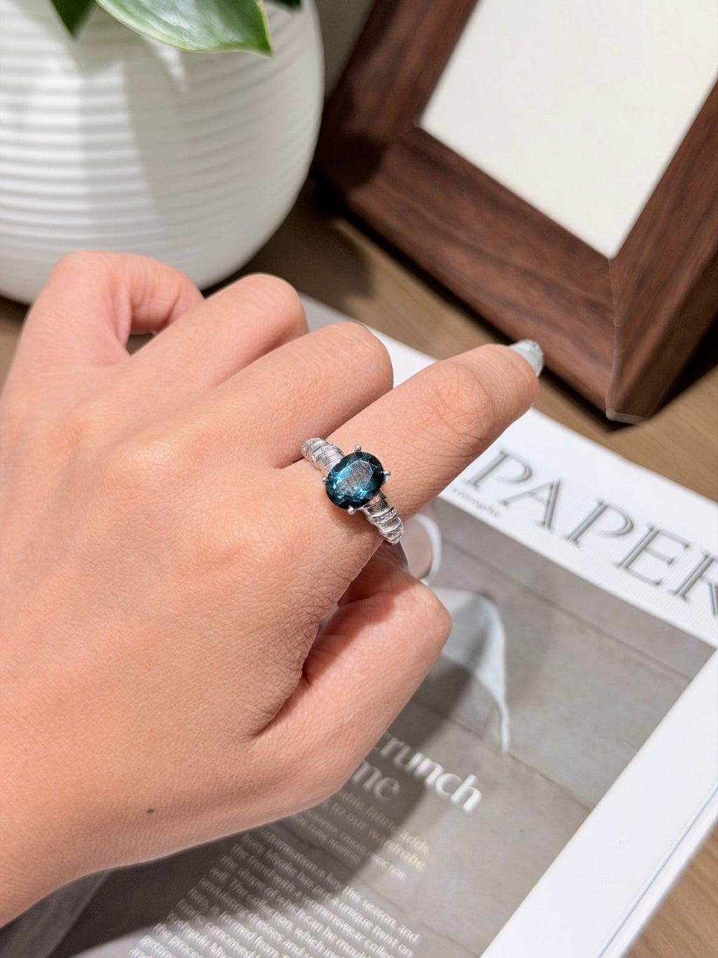 Hand wearing a silver-tone ring with a dark blue oval gemstone