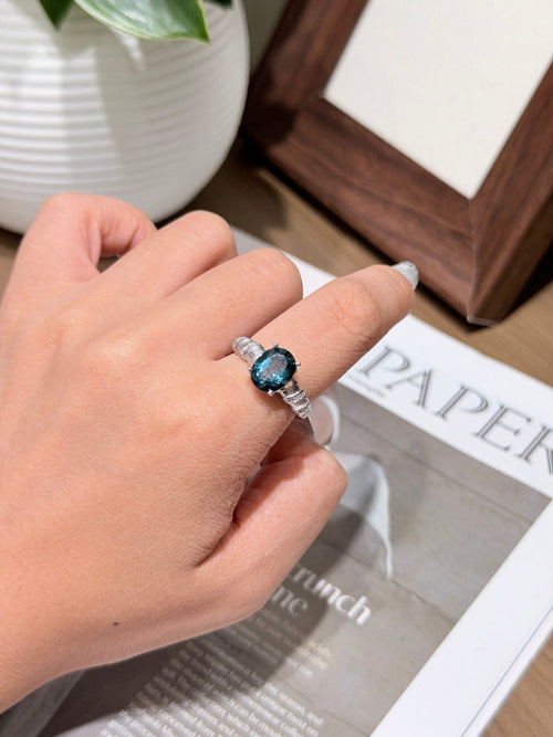 Hand wearing a silver-tone ring with a dark blue oval gemstone