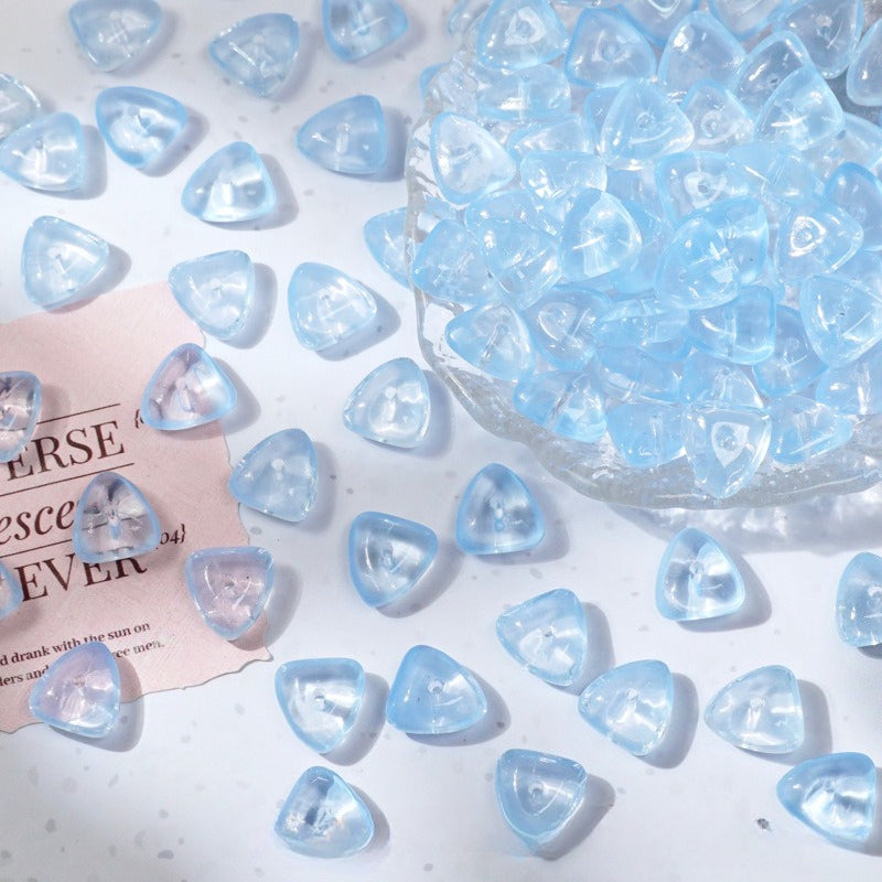 Light blue translucent triangle-shaped glass beads on a white surface with a clear glass bowl of beads