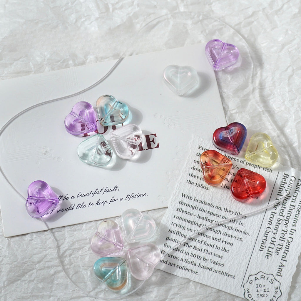 Translucent heart-shaped glass beads in pastel and bright colors on a white textured fabric with decorative cards