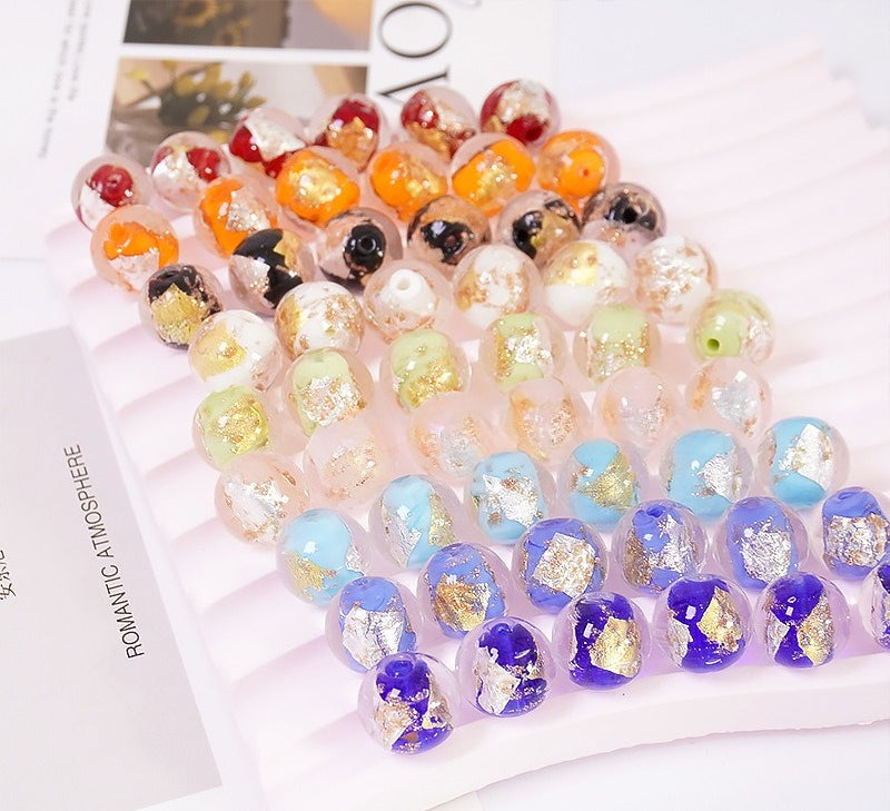 Multicolor gold and silver foil-effect glass round beads arranged on a white striped tray