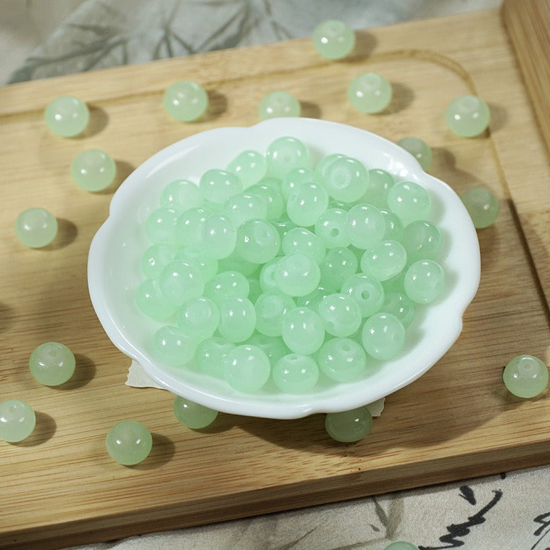 Light green imitation jade glass beads in a small white dish on a wooden board