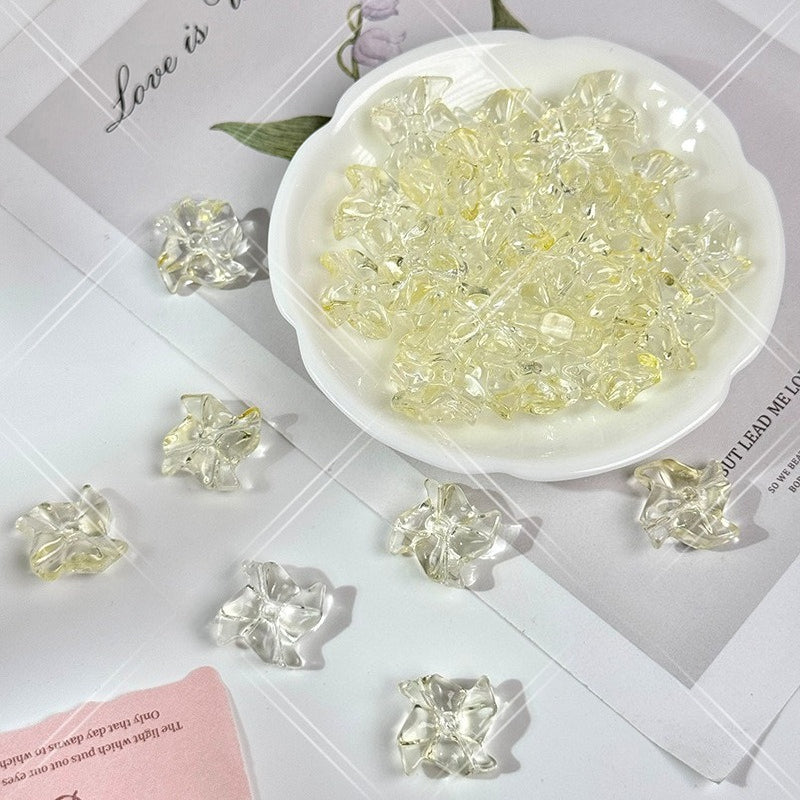 Clear 20mm carved glass windmill beads with a pale yellow tint, shown in a small white dish on a styled flat-lay background
