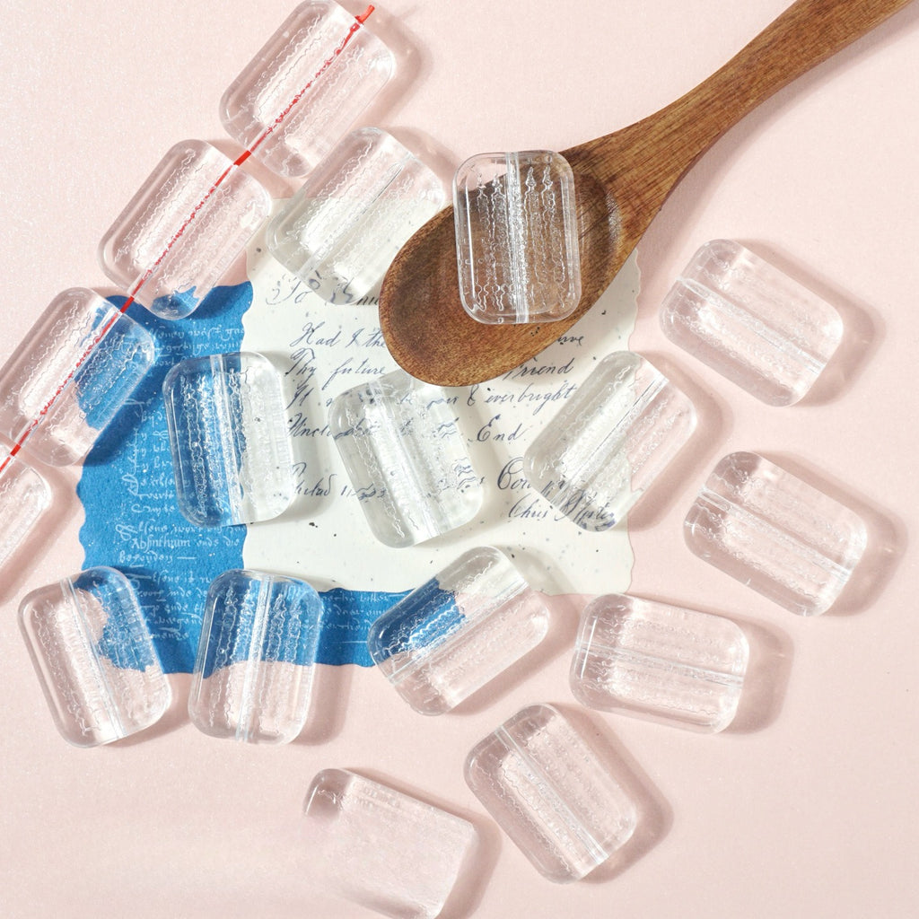 Clear rectangular glass beads like miniature ice cubes on pink with a wooden spoon and vintage cards