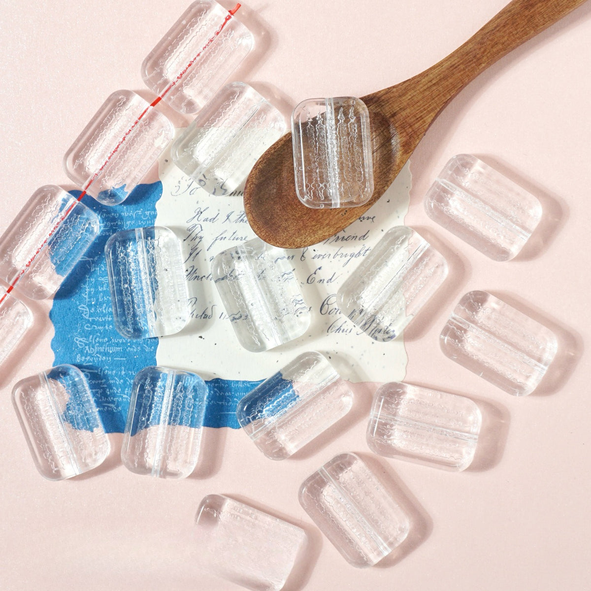 Clear rectangular glass beads like miniature ice cubes on pink with a wooden spoon and vintage cards