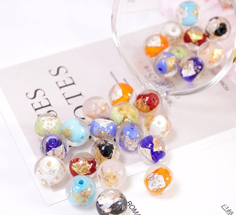 Multicolor gold-leaf glass beads scattered on a card beside a glass bowl