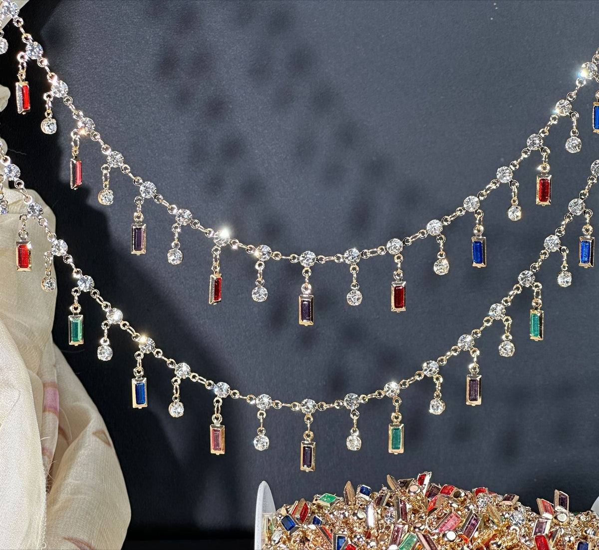 Gold-tone tassel chain with clear rhinestones and dangling rectangular crystals in red, blue, green, and purple