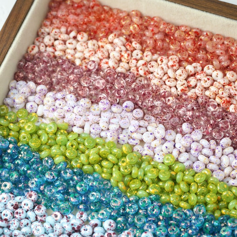 Colorful 3x6mm Picasso-finish glass abacus beads in diagonal rows in a tray, blue, green, yellow, pink, and red tones.