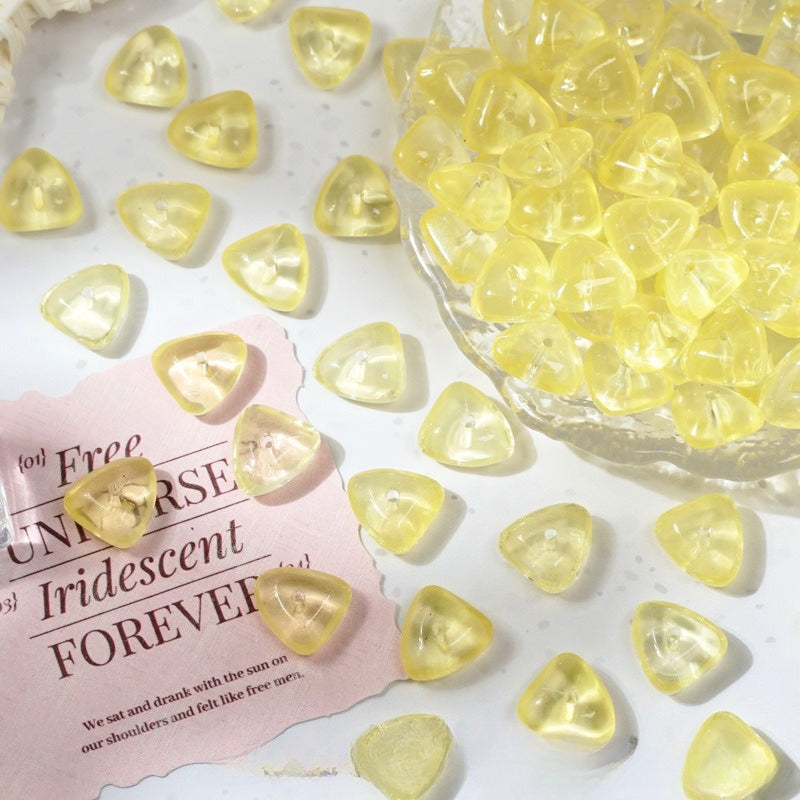 Yellow iridescent heart-shaped glass beads scattered on a white surface with a glass bowl