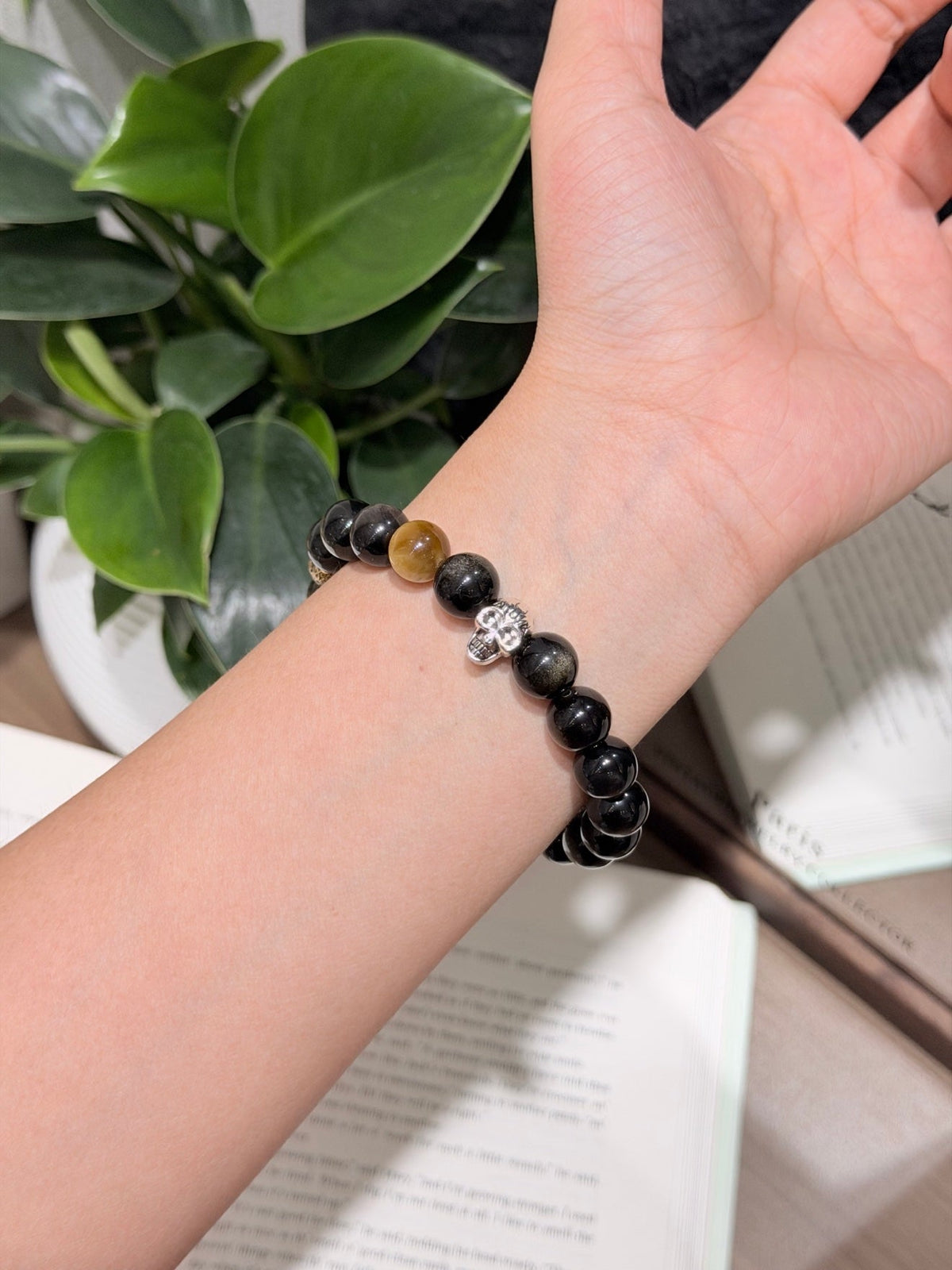 Wrist wearing black beaded bracelet with brown stone bead and silver skull charm