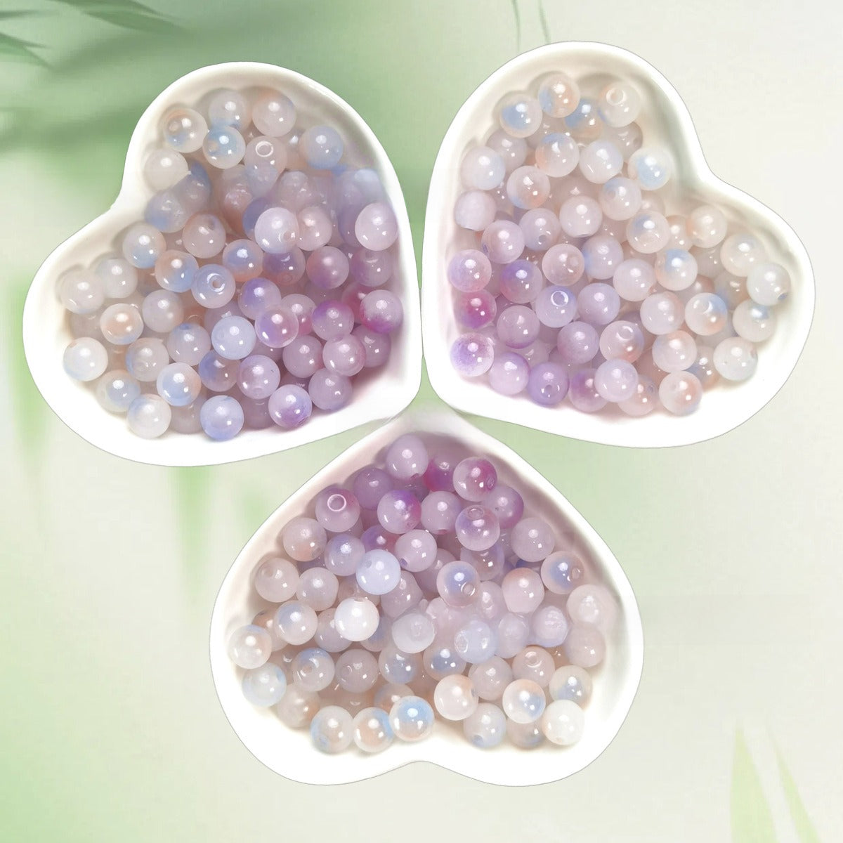 Three heart-shaped bowls of iridescent pastel lavender, lilac, and pale blue beads