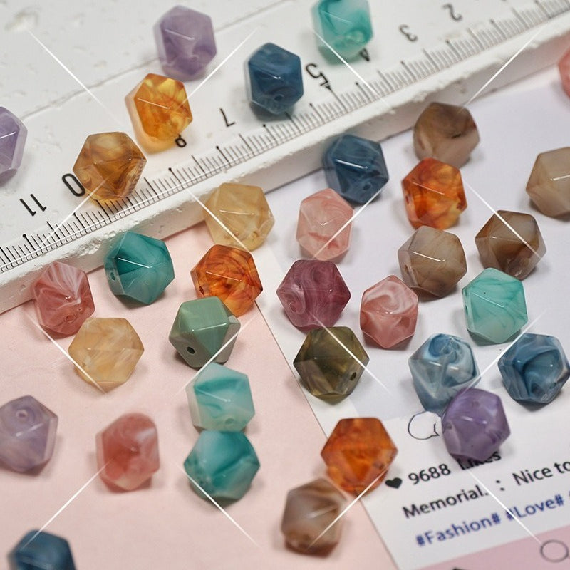A collection of faceted gemstone beads in various colors and patterns, arranged on a pink background with a white ruler for scale.