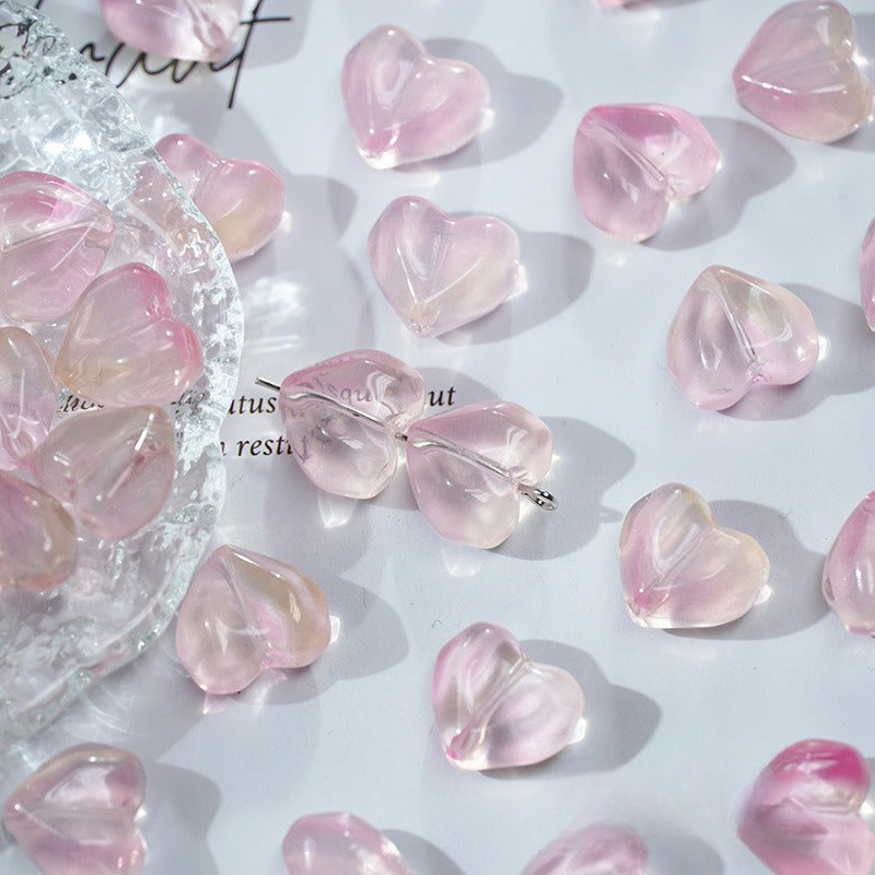 Translucent pink heart-shaped glass beads on a white surface with a clear textured glass dish on the left