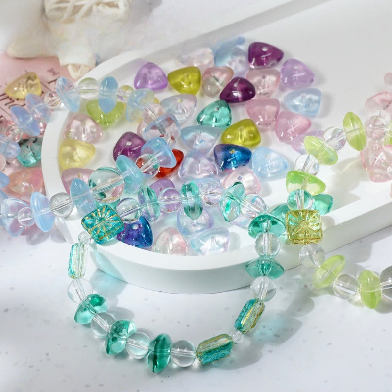 Pastel heart-shaped glass beads and translucent faceted beads on a white tray with a green beaded bracelet