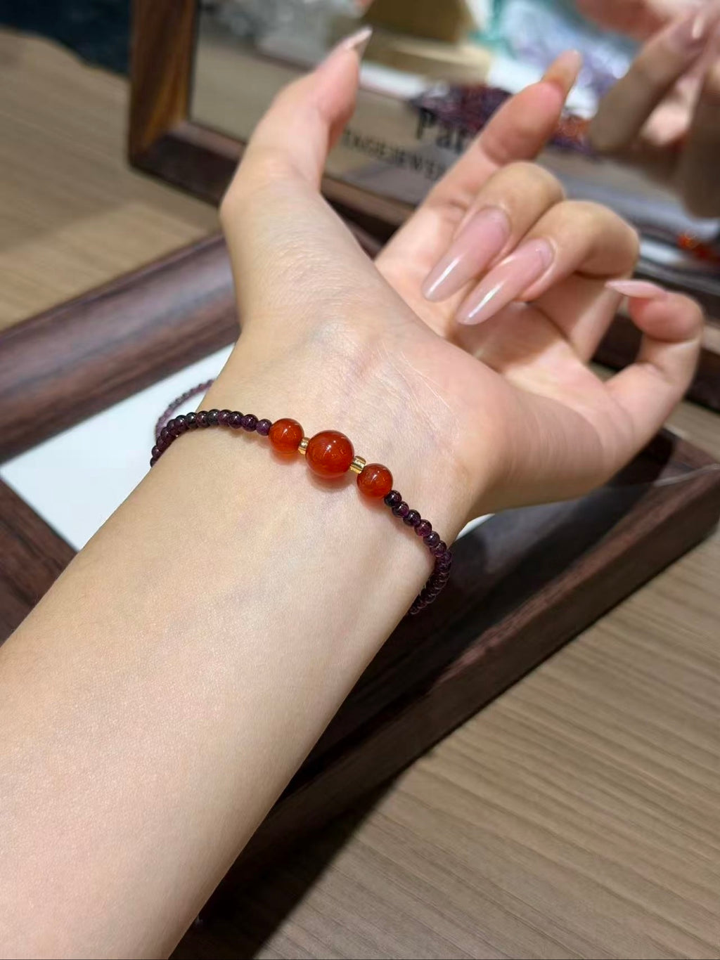 Wrist wearing the purple garnet and carnelian bracelet set, hand resting by a wooden tray