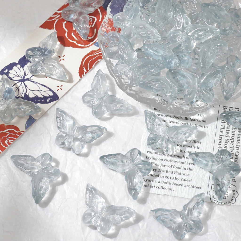 Clear butterfly-shaped glass beads scattered on white textured surface with glass bowl