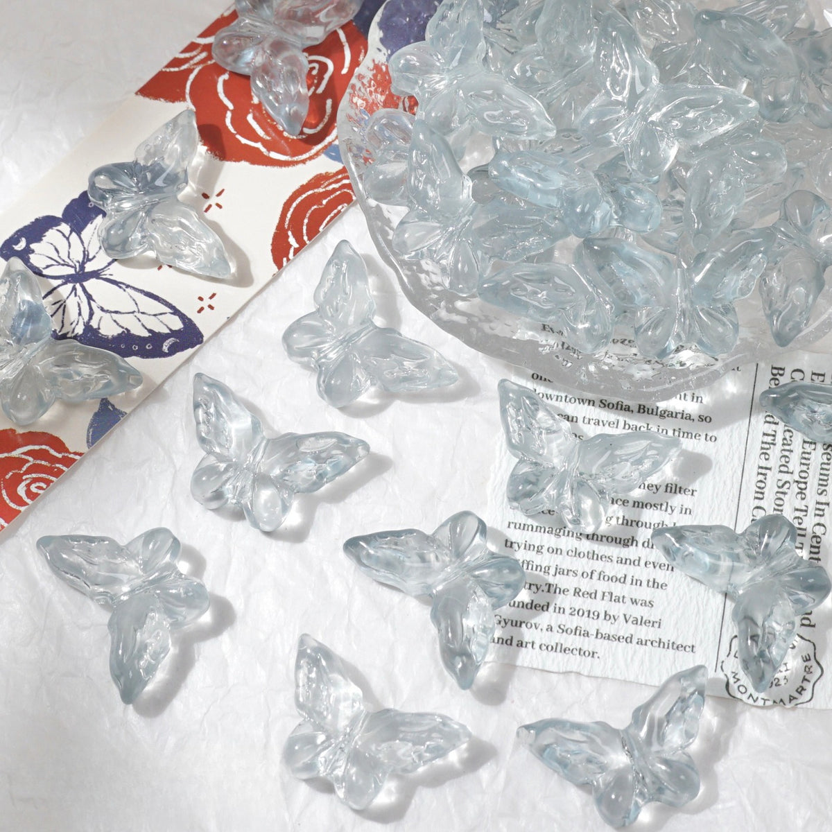 Clear butterfly-shaped glass beads scattered on white textured surface with glass bowl
