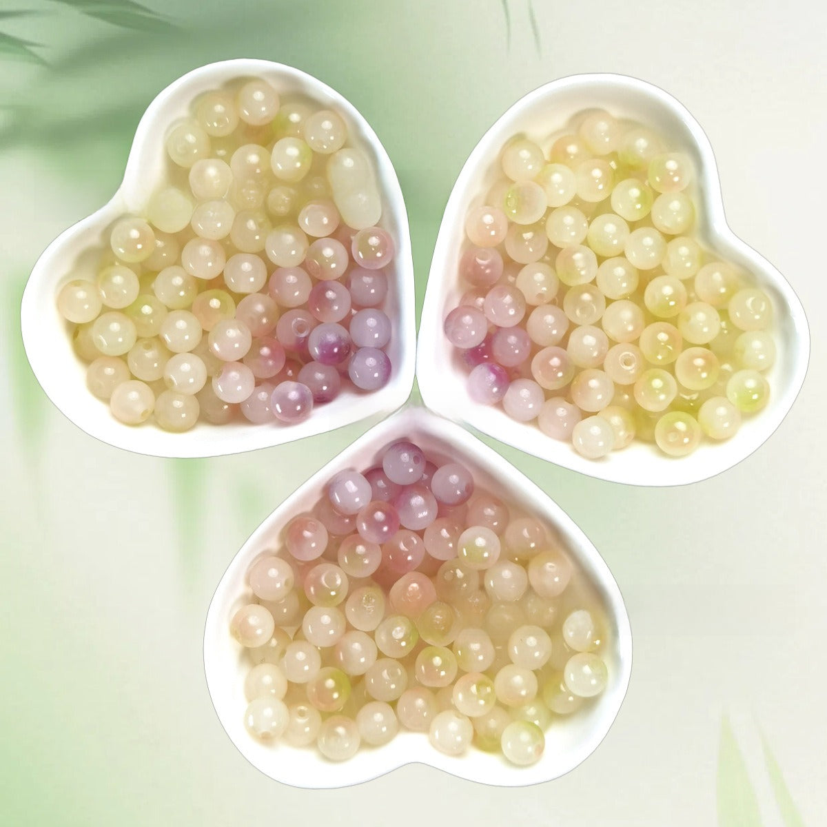 Three heart-shaped bowls of translucent pearl-like pastel beads on pale green