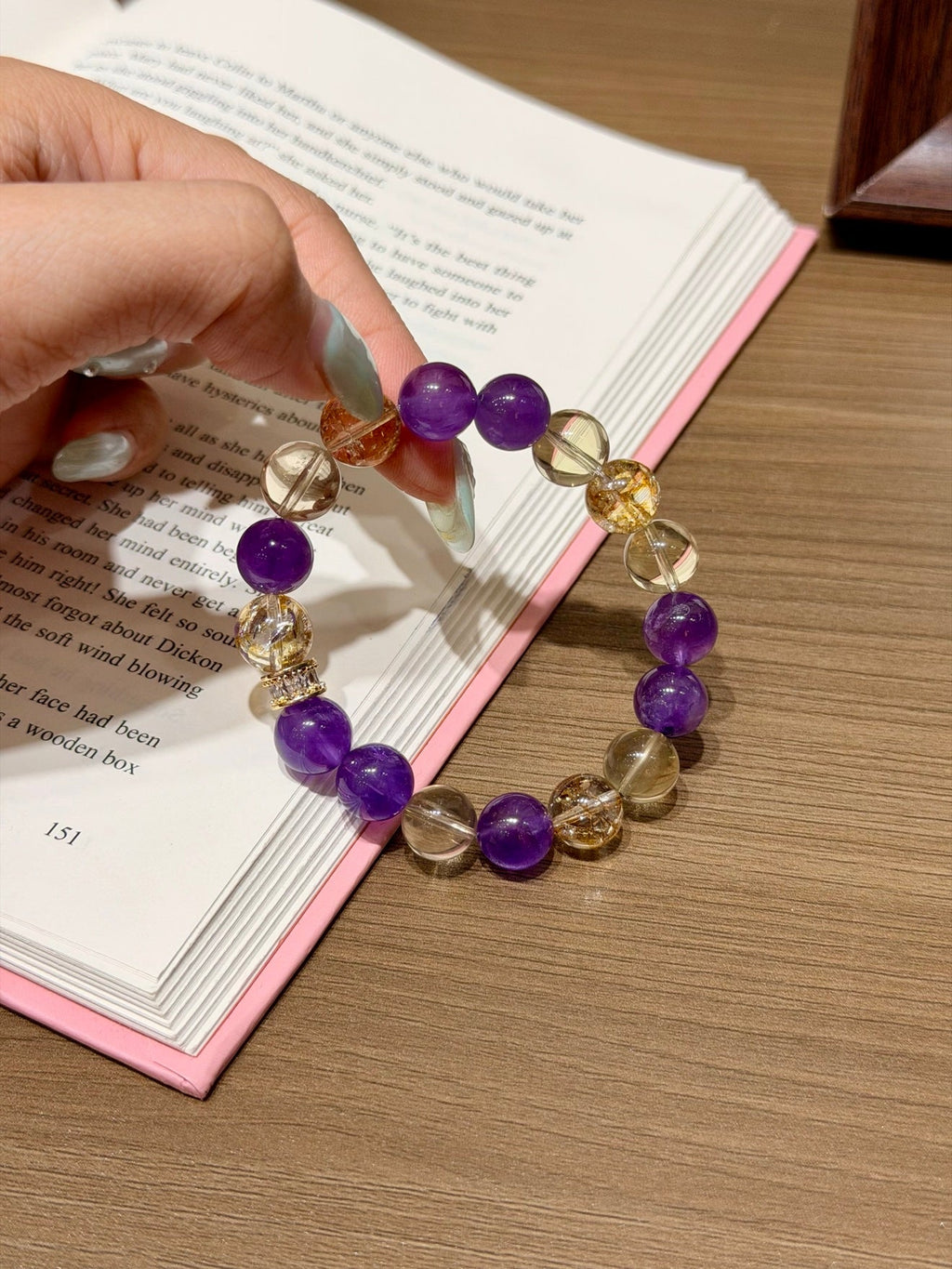 Hand holding purple amethyst and gold citrine beaded bracelet over an open book