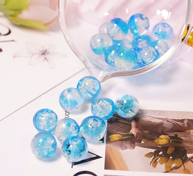 Light blue two-tone glow-in-the-dark glass beads spilling from a glass cup onto a printed card