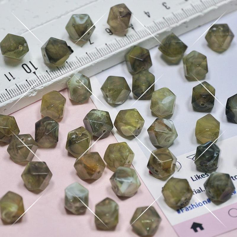Faceted olive-green and brown beads scattered on a pink and white surface with a ruler