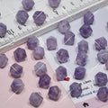 Small faceted purple beads scattered on a pink and white surface with a ruler
