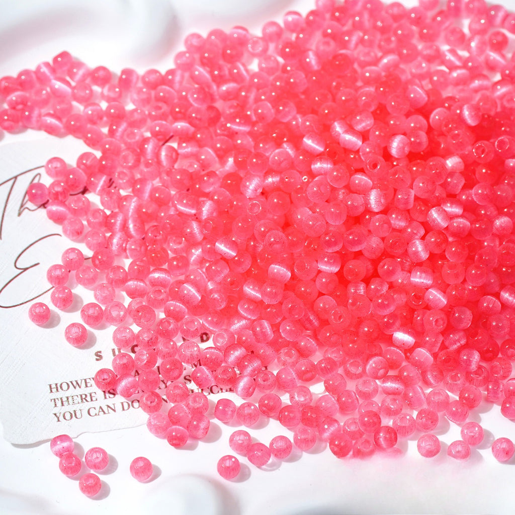 Close-up pile of frosted pink cat's-eye glass beads on white surface