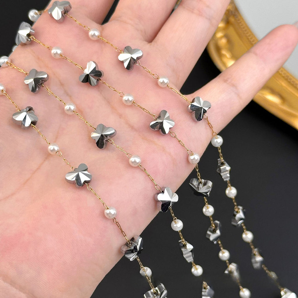 Gold chain strands with silver butterfly charms and white pearls draped across an open hand