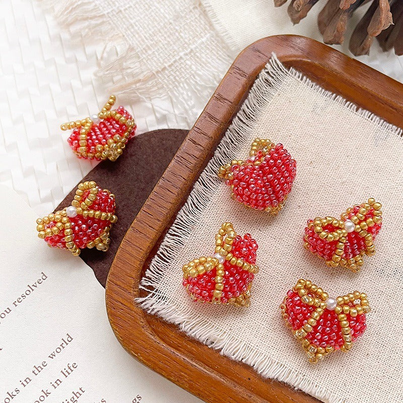 Red and gold beaded apple charms with pearl accents on a wooden tray with white fabric