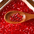 Red glazed glass long rice beads in a wooden spoon