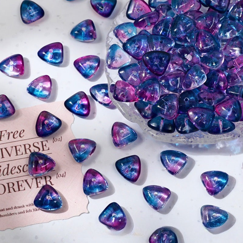 Galaxy blue and purple triangle glass beads scattered on a white surface with a glass bowl