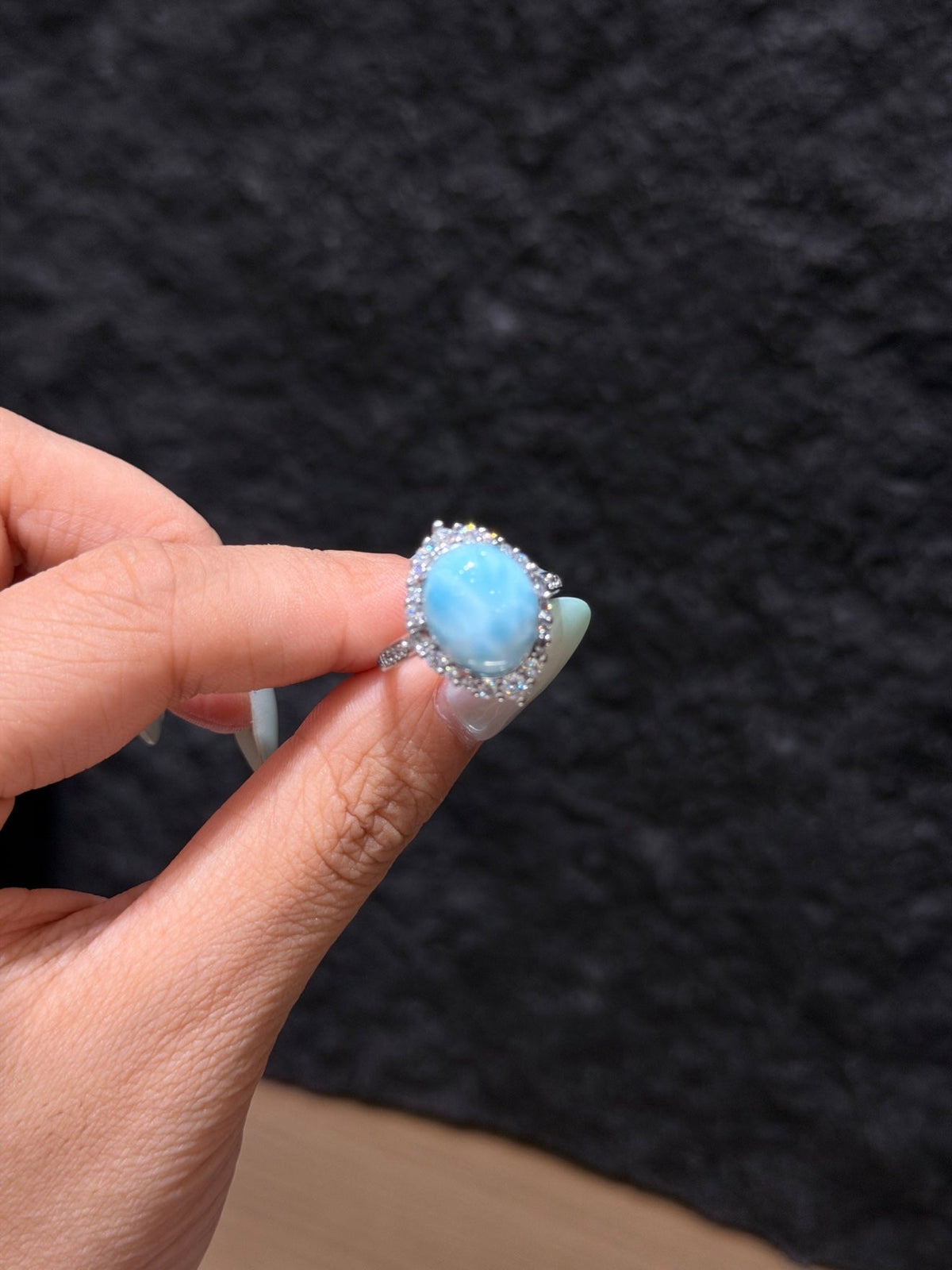 Hand holding an oval light blue larimar ring with a clear stone halo