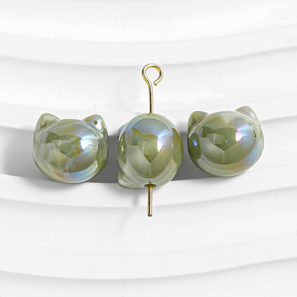 Three iridescent green cat-shaped stud earrings with gold hooks on a white wavy surface.