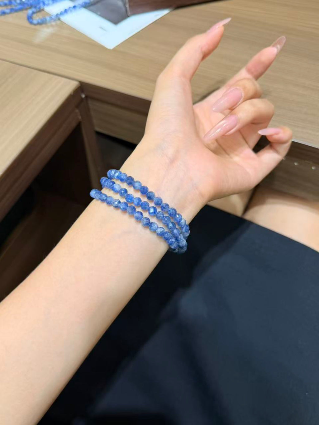 Hand with a blue faceted kyanite beaded bracelet wrapped multiple times around the wrist, with another bead strand resting on the table behind.