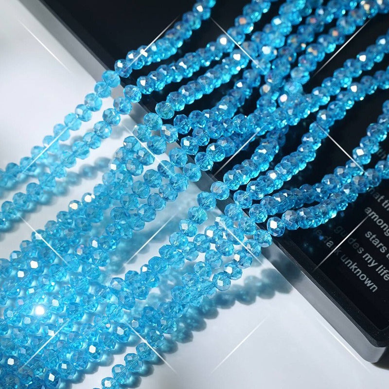Strands of faceted light blue crystal glass wheel beads on white surface beside black book edge