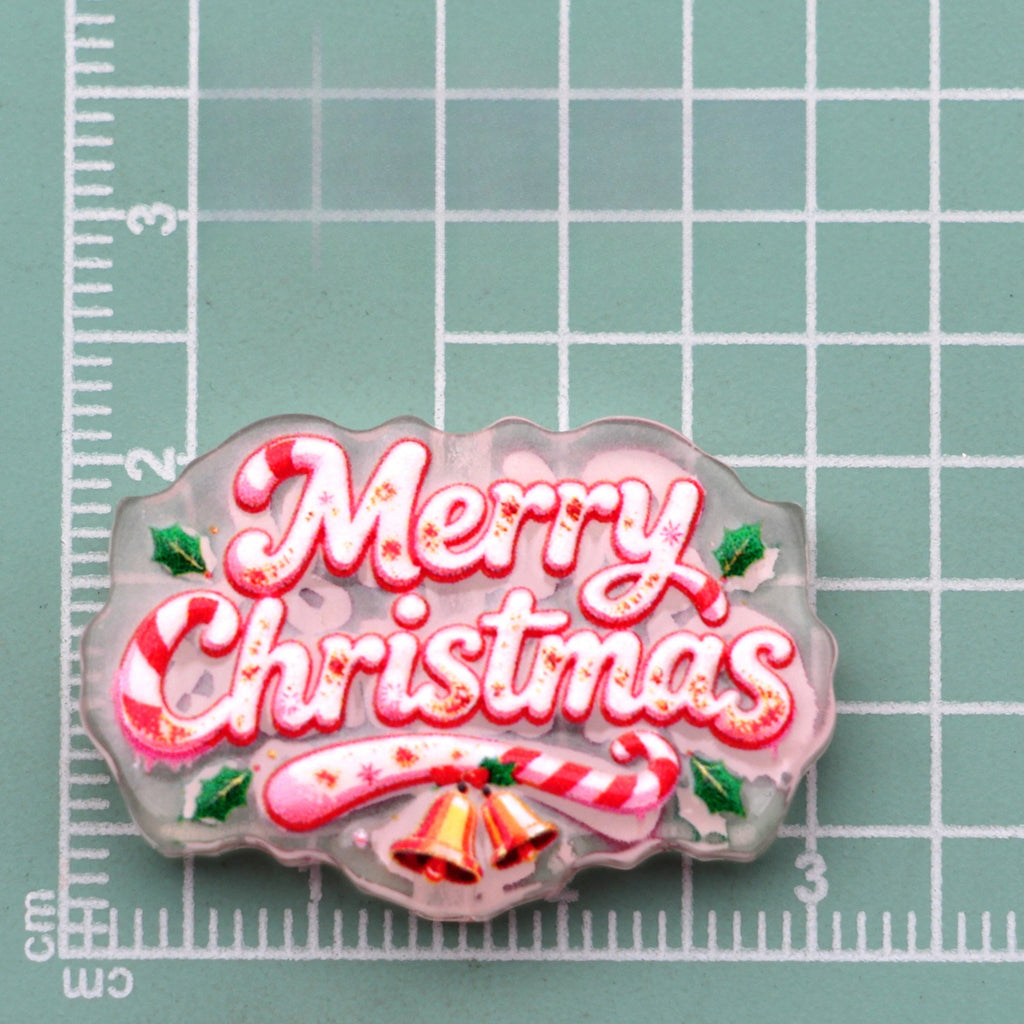Merry Christmas script acrylic charm with candy canes, holly, and gold bells on green cutting mat